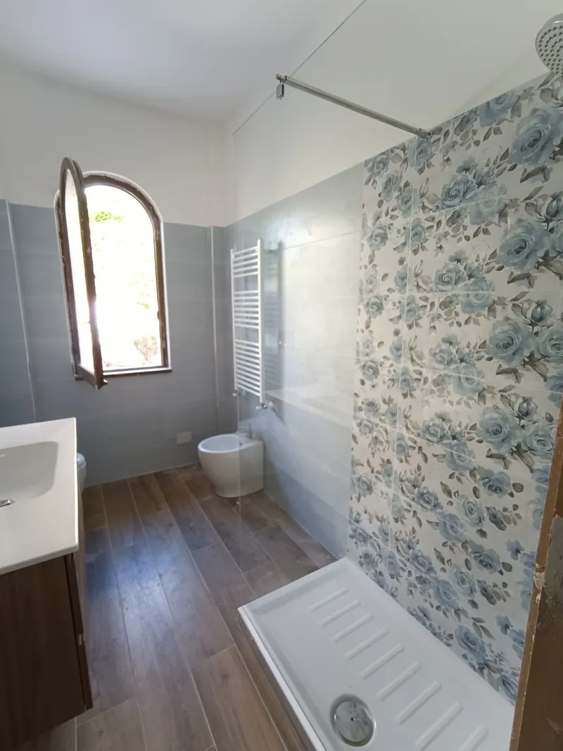 Bagno con piatto doccia, rivestimento decorato e pavimento effetto legno